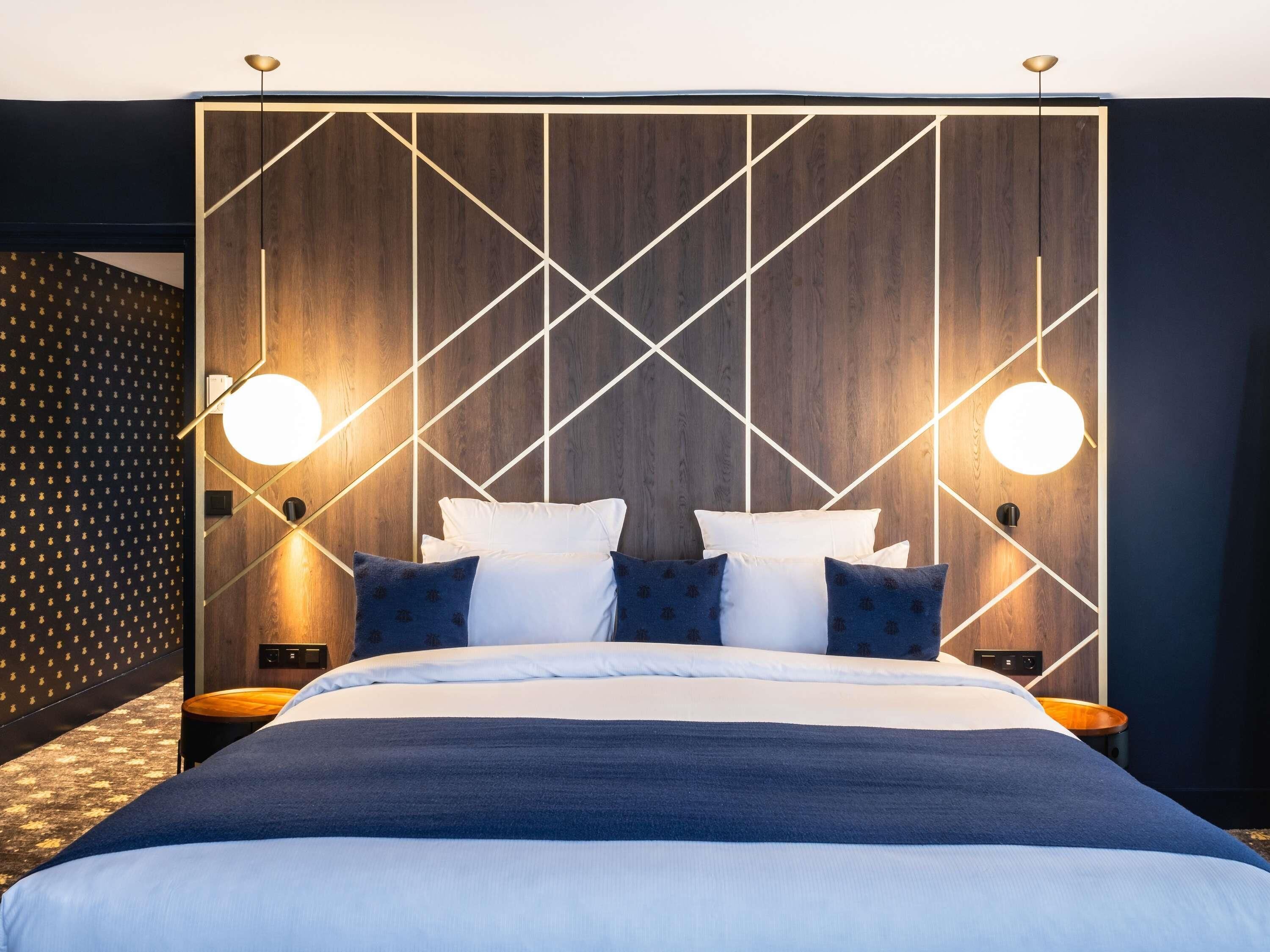 Una habitación de hotel moderna con una cama grande, dos mesitas de noche y un cabecero con estampado geométrico.