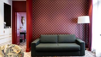 Una habitación con un sofá verde oscuro, un sillón estampado, un jarrón decorativo y una pared con diseño.