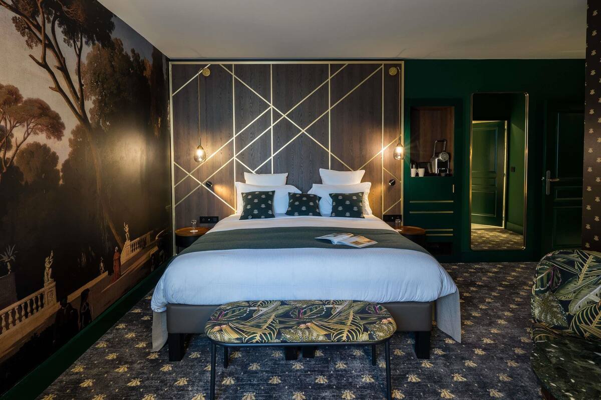 Quarto de hotel moderno com uma cama grande, um banco e uma parede verde decorativa.