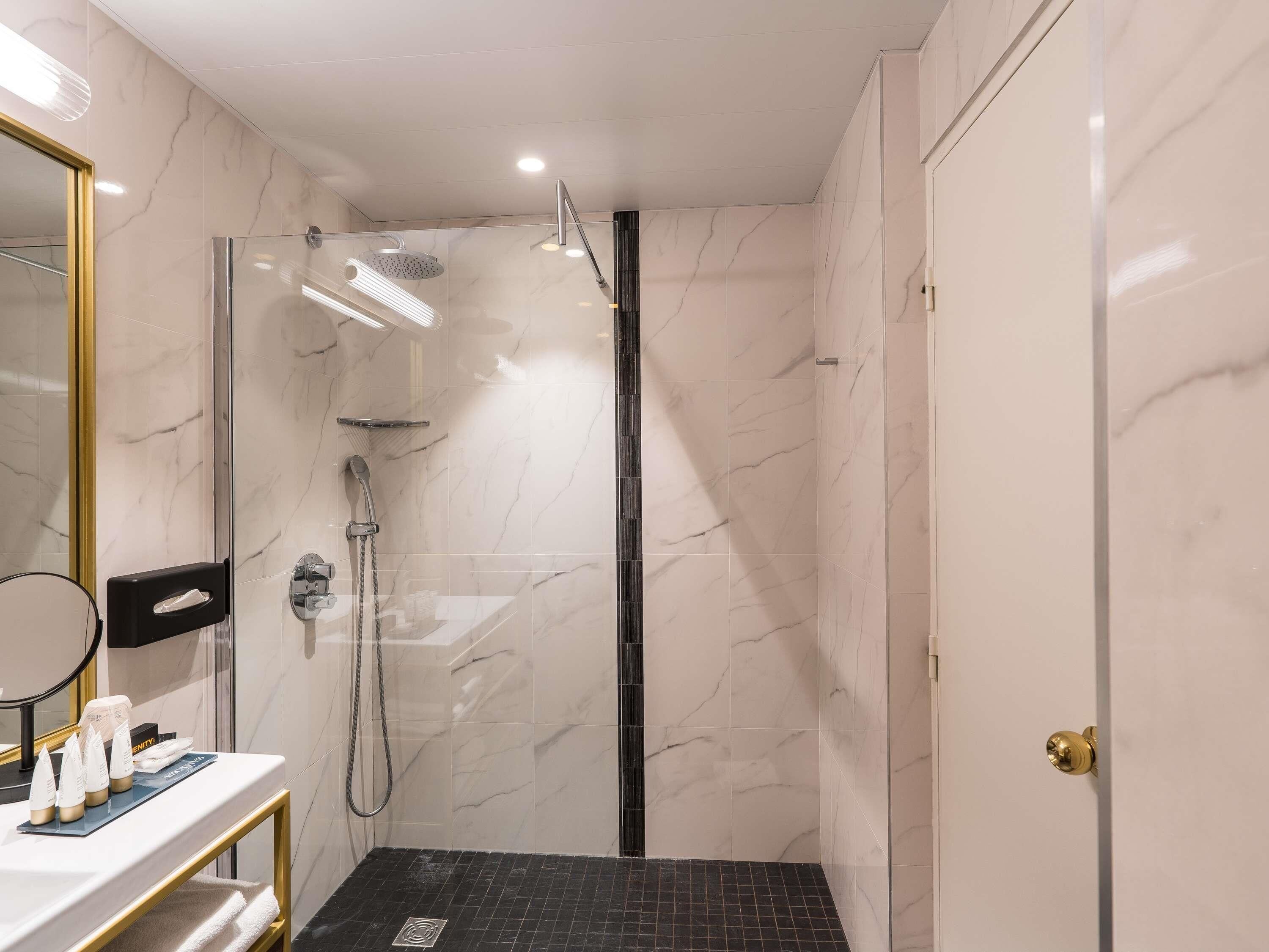 A modern bathroom with a glass-enclosed shower, a vanity with toiletries, and a marble-tiled wall.
