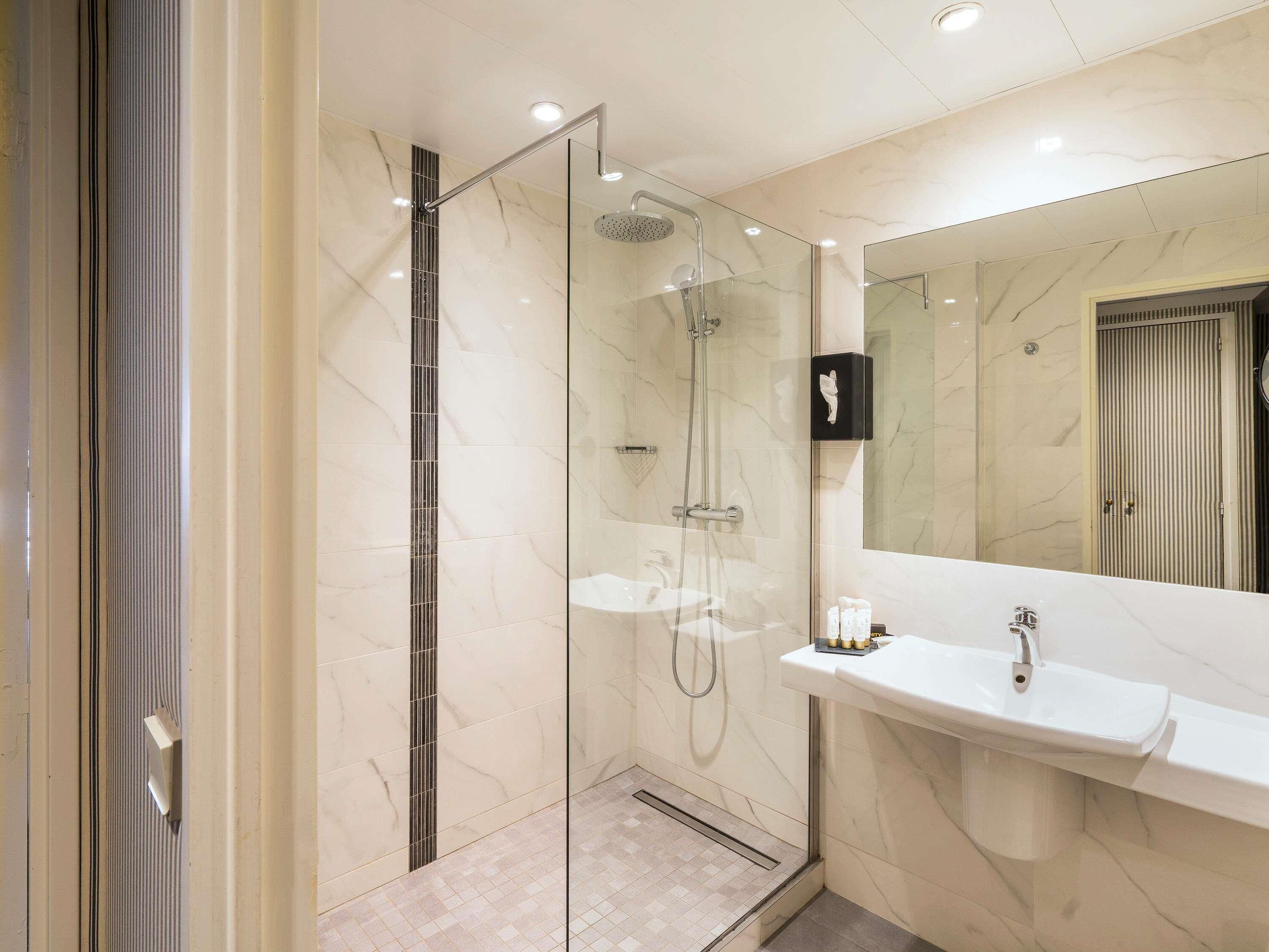 A modern bathroom with a glass-enclosed shower, a marble sink, and a large mirror.