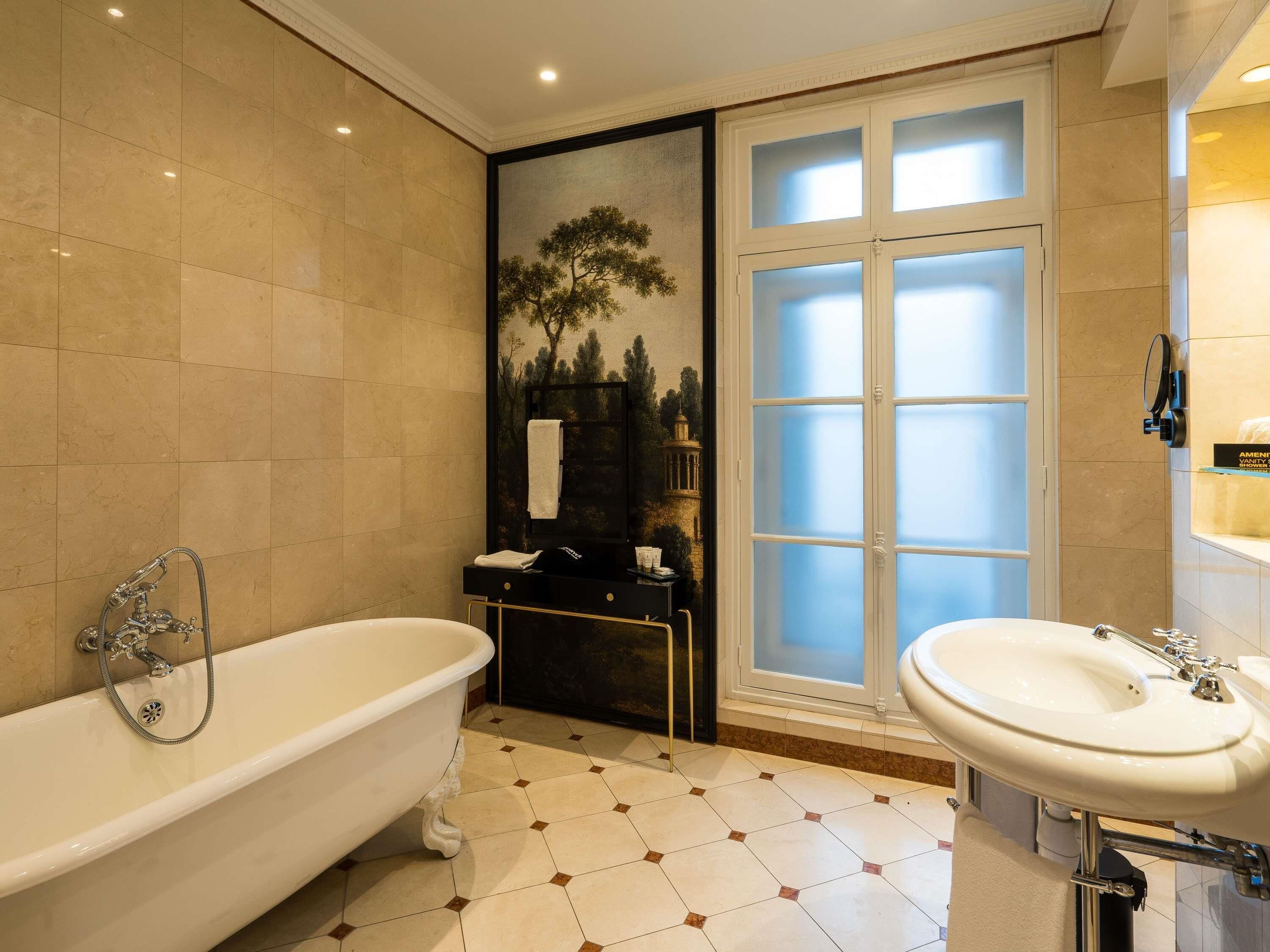 Un baño con una bañera independiente, un lavamanos, un espejo y un ventanal con cristal satinado.