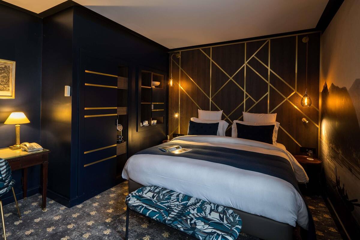 Quarto de hotel moderno com uma cama grande, mesas de cabeceira, uma escrivaninha e um banco.