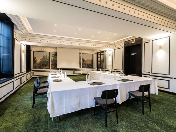 Un salón de conferencias con una larga mesa, sillas y una pantalla de proyector.