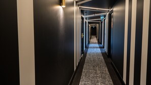 Un long couloir étroit, doté d’un sol recouvert de moquette et de murs peints de bandes noires et blanches alternées.