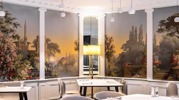 A dining room with a large mural, a central table with chairs, and pendant lighting.