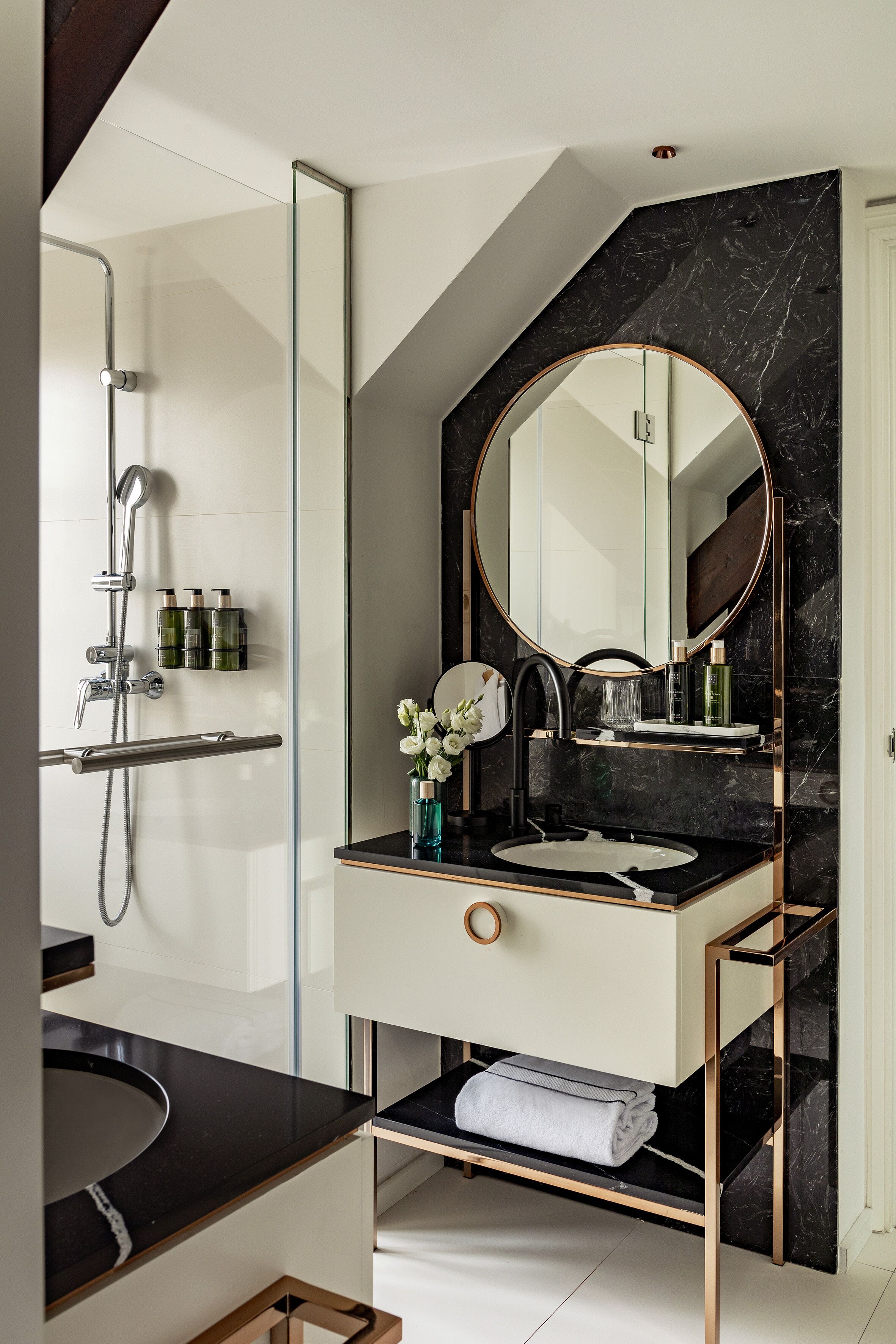 A modern bathroom with a black marble wall, a round mirror, a sink, and a shower.