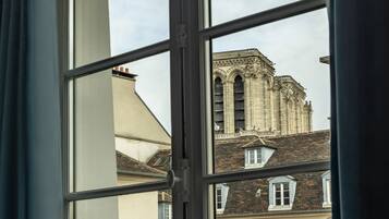 Une fenêtre donnant sur un bâtiment à l’architecture particulière, un balcon avec une rambarde en métal et un rideau partiellement visible.