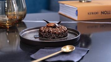 Un dessert servi dans une assiette, accompagné d’une cuillère, d’un livre et de lunettes, le tout posé sur une table.