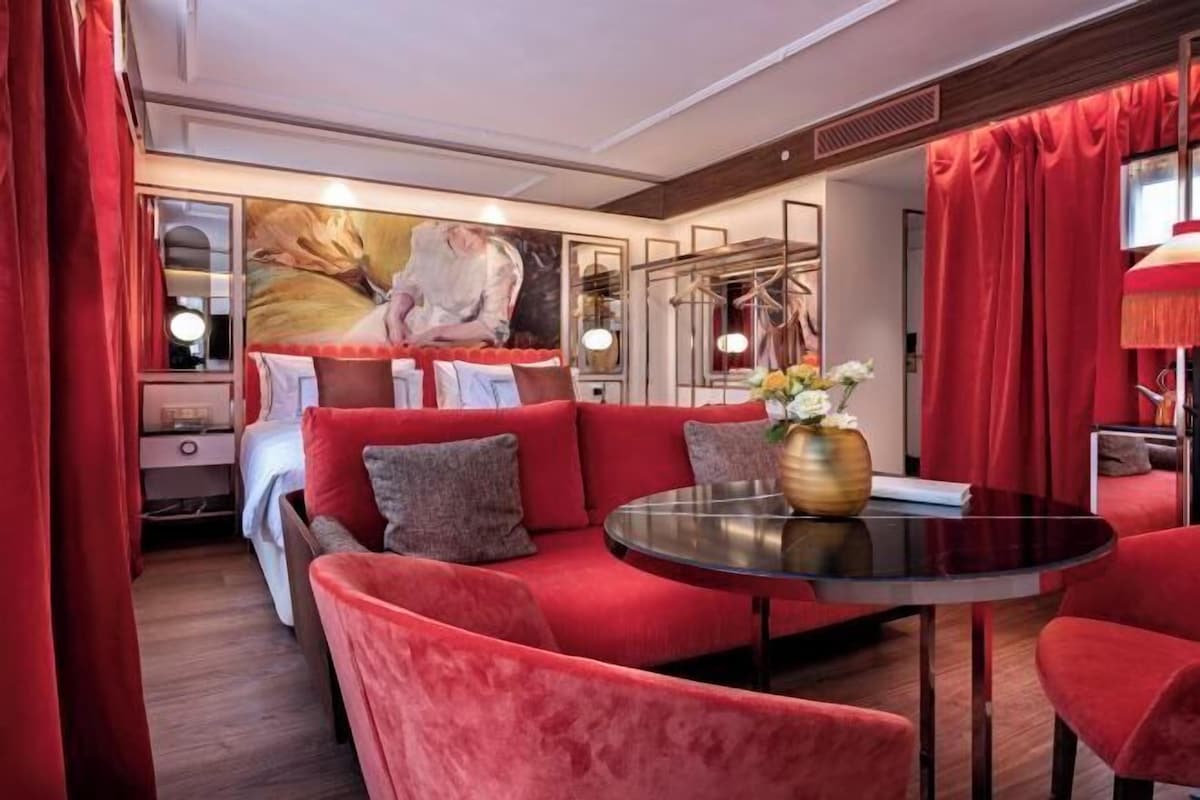 A modern hotel room with a red sofa, a round table, and a large painting on the wall.