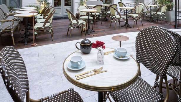 An outdoor cafe with tables and chairs, surrounded by white buildings with balconies. - Maison Colbert, member of Meliá Collection  Notre-Dame (Paris)