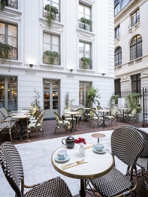 An outdoor cafe with tables and chairs, surrounded by white buildings with balconies.