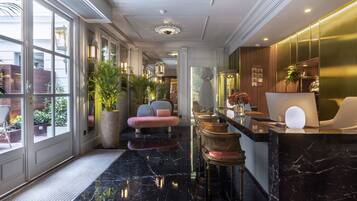 Een moderne hotel lobby met een marmeren vloer, een zithoek met gestoffeerde stoelen, een receptiebalie en grote ramen met uitzicht op buiten.