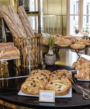 A bakery display with various breads and pastries, including croissants and a label indicating 'Pain aux raisins'. - Maison Colbert, member of Meliá Collection  Notre-Dame (Paris)