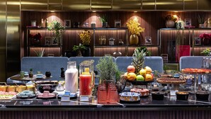 A buffet with a variety of food and drinks, including fruits, pastries, and beverages, set against a backdrop of wooden paneling and blue upholstered seating. - Maison Colbert, member of Meliá Collection  Notre-Dame (Paris)