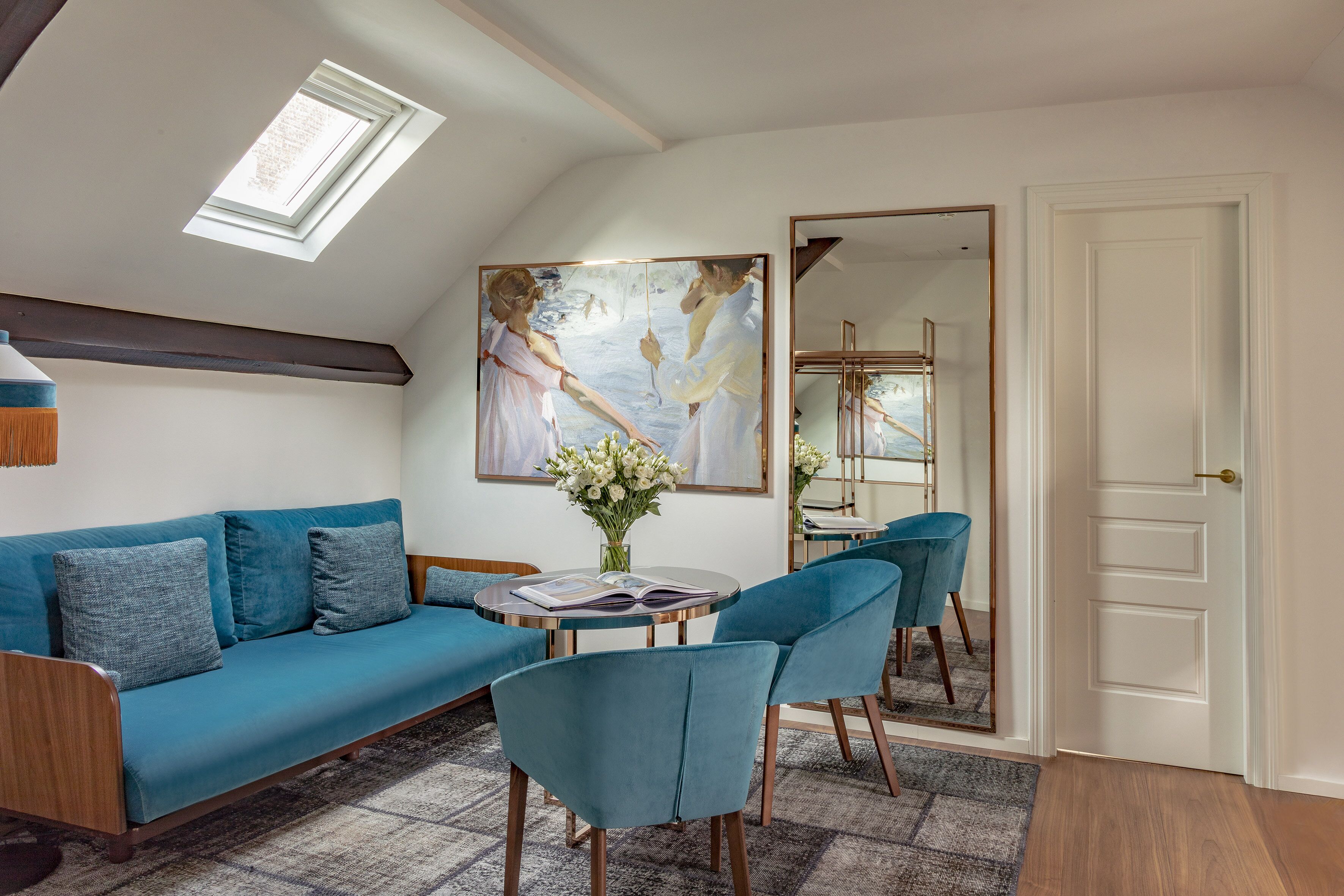 A modern living room with a blue sofa, matching chairs, a round coffee table, and a large painting.