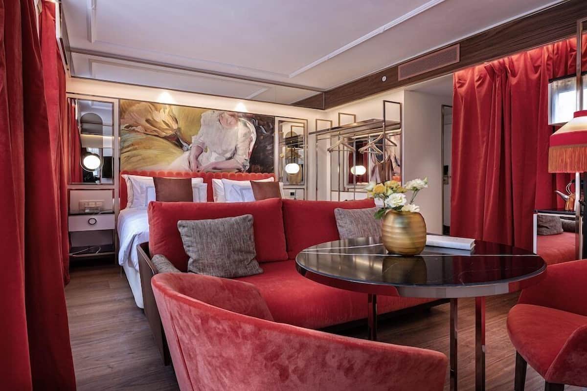A modern hotel room with a red sofa, a round table, and a large mirror.