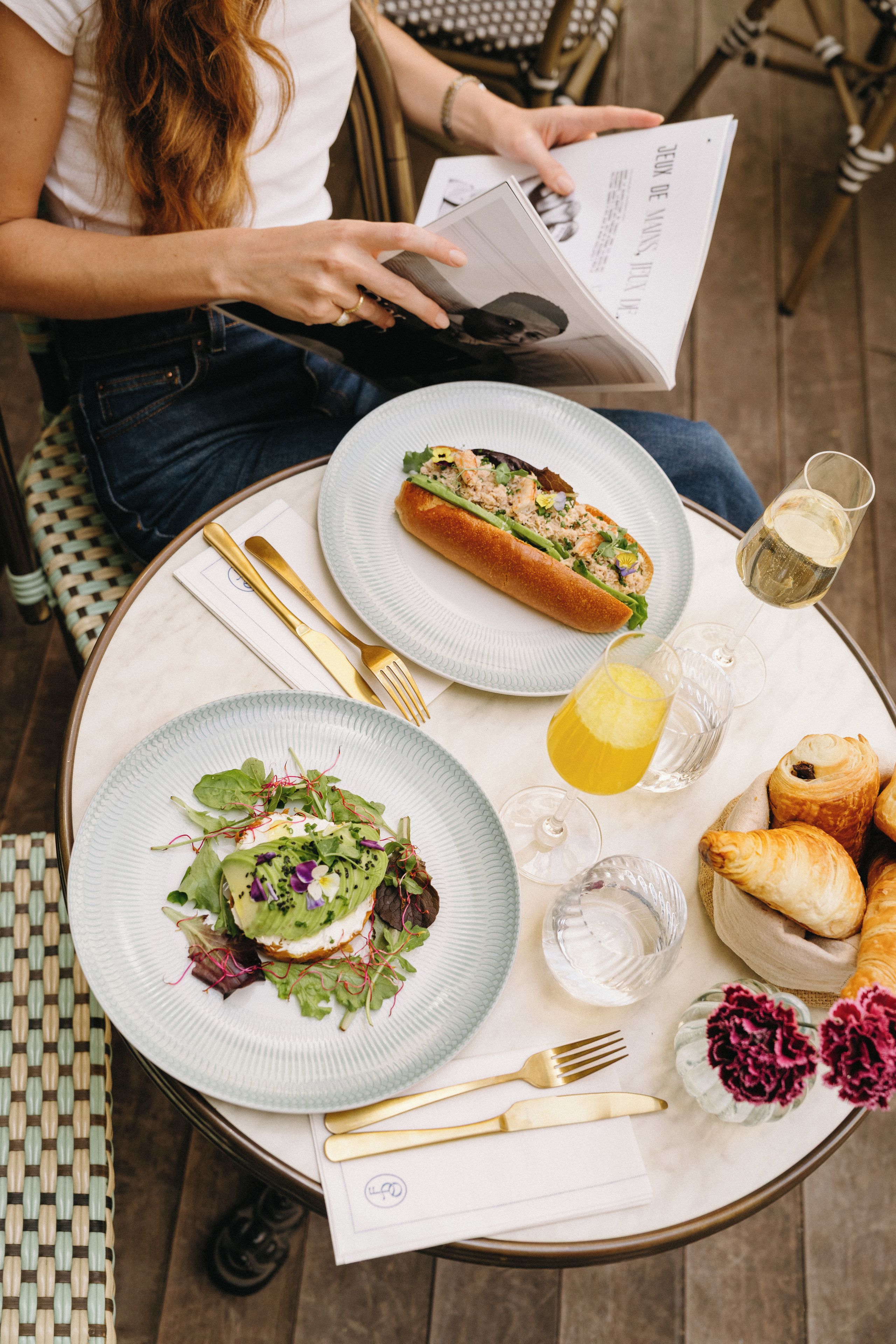 A table set with a meal, including a sandwich, salad, and pastries, with a glass of white wine and a lemon.