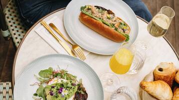 A table set with a meal, including a sandwich, salad, and pastries, with a glass of white wine and a lemon.