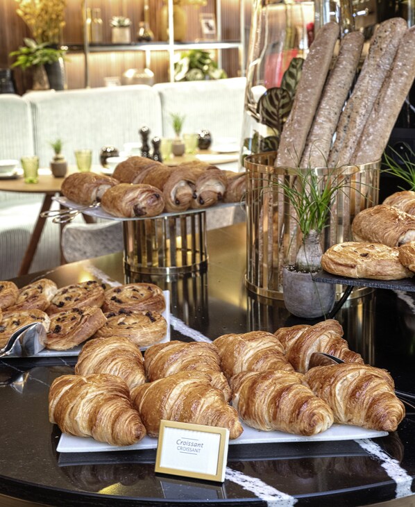 Una exhibición de diversos pasteles y panes, incluyendo cruasanes y barras, dispuesta sobre una mesa en un café.