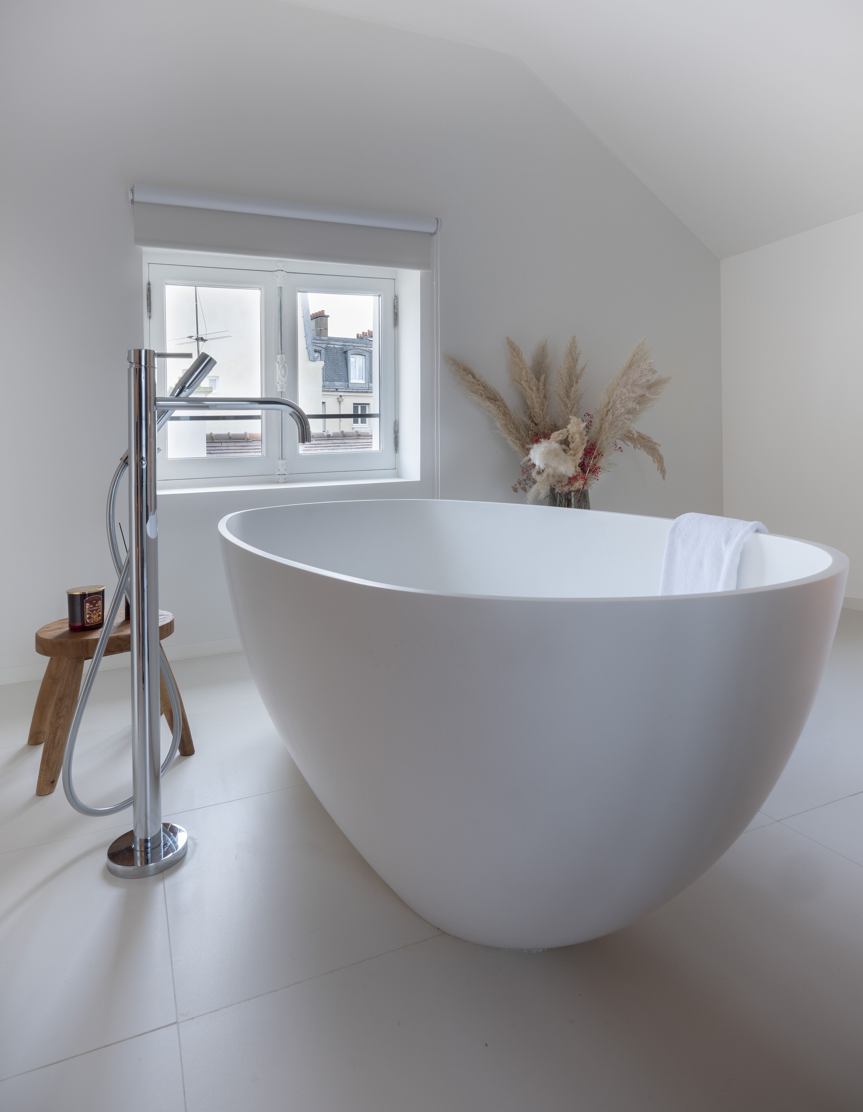 Un baño moderno con una bañera blanca grande, un grifo cromado y un taburete de madera.
