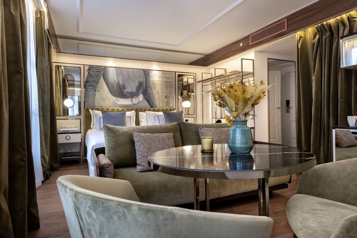 A modern hotel room with a sofa, a round table, and a large painting on the wall.