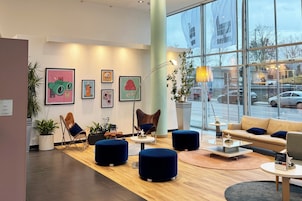 Un moderno vestíbulo de hotel con piso de madera, otomanas azules, un sofá color crema y obras de arte en las paredes.