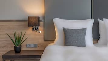 A modern hotel room with a neatly made bed, a bedside table with a lamp, and a potted plant.