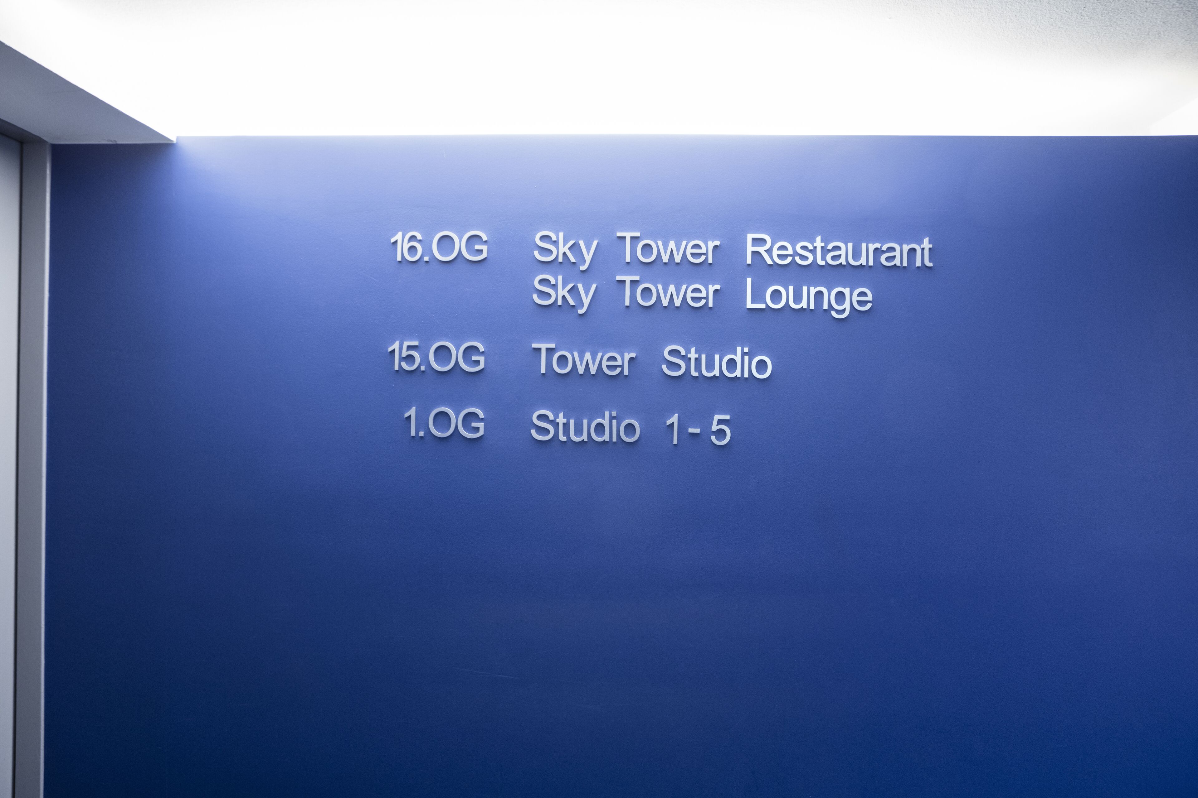 A blue wall with white text listing room numbers and names: 16.0G Sky Tower Restaurant, 15.0G Sky Tower Lounge, 15.0G Tower Studio, 1.0G Studio 1-5.