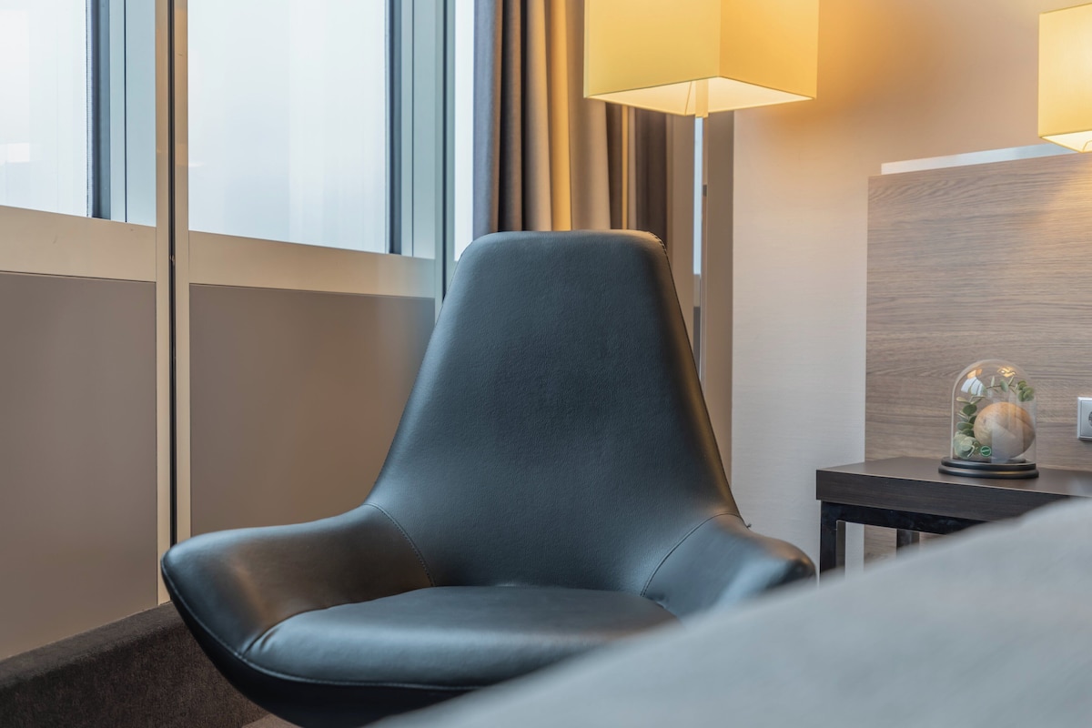 A modern hotel room with a leather armchair, a lamp, and a decorative globe on a side table.