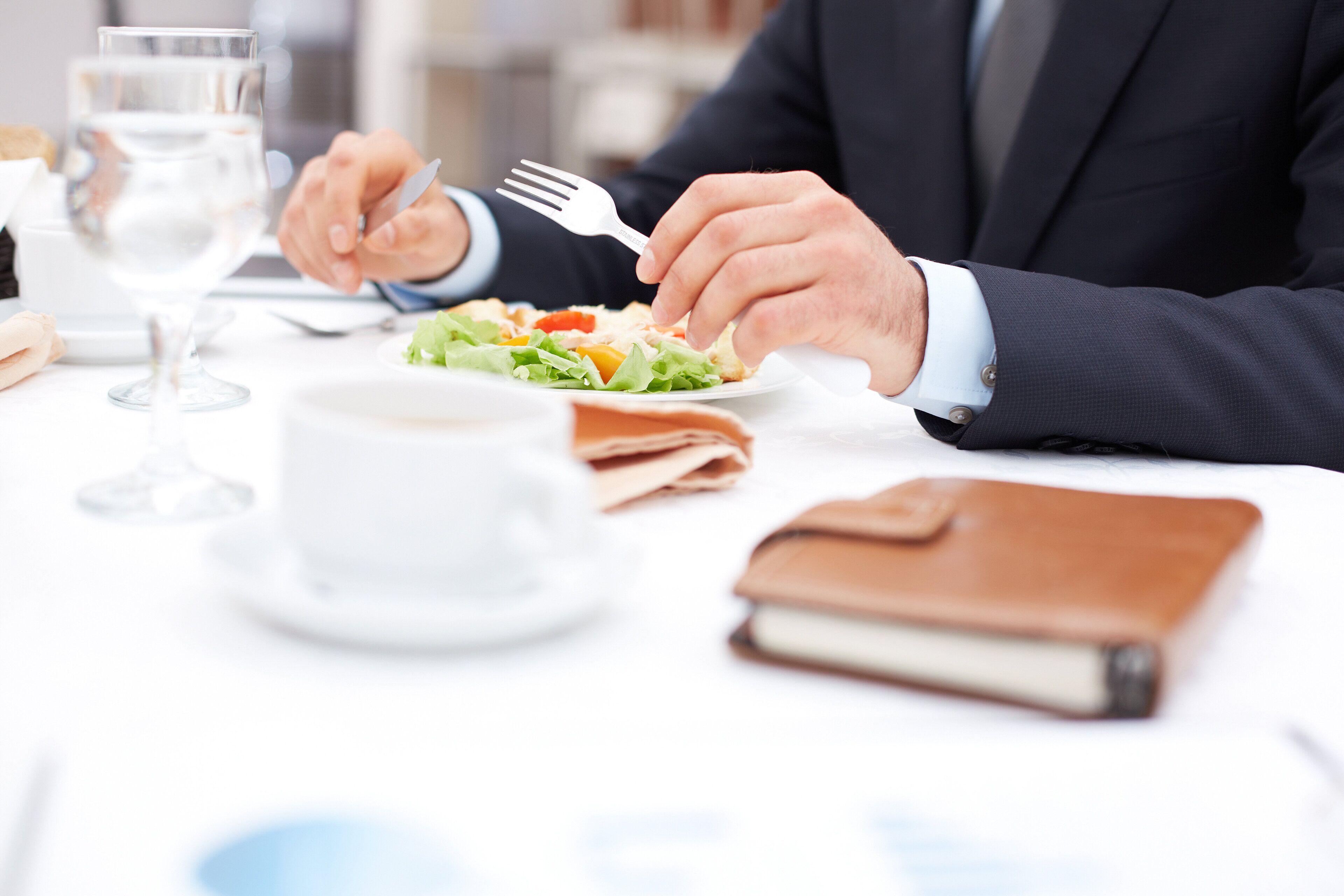 A person in a dark suit dining at a table with a salad, a glass of water, and a notebook.