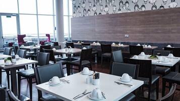 Un restaurante con varias mesas y sillas, cada conjunto con platos blancos, cubiertos y una taza blanca.