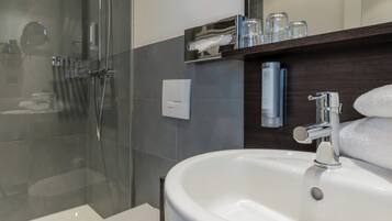 A modern bathroom with a glass-enclosed shower, a white sink, and a mirror above the sink.