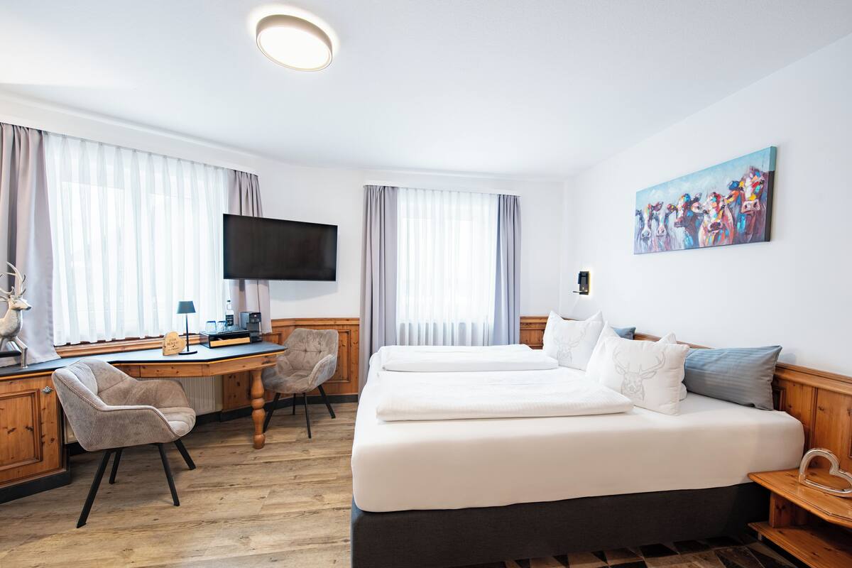 A hotel room with a large bed, a desk with a chair, a TV, and a painting on the wall.