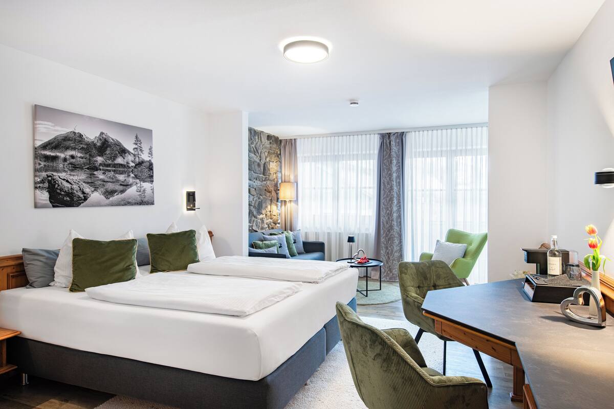 A hotel room with a large bed, two chairs, a small table, and a painting on the wall.