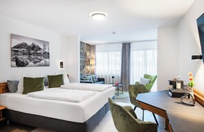 A hotel room with a large bed, two chairs, a small table, and a painting on the wall. - Mäser's Allgäuherz (Wiggensbach)