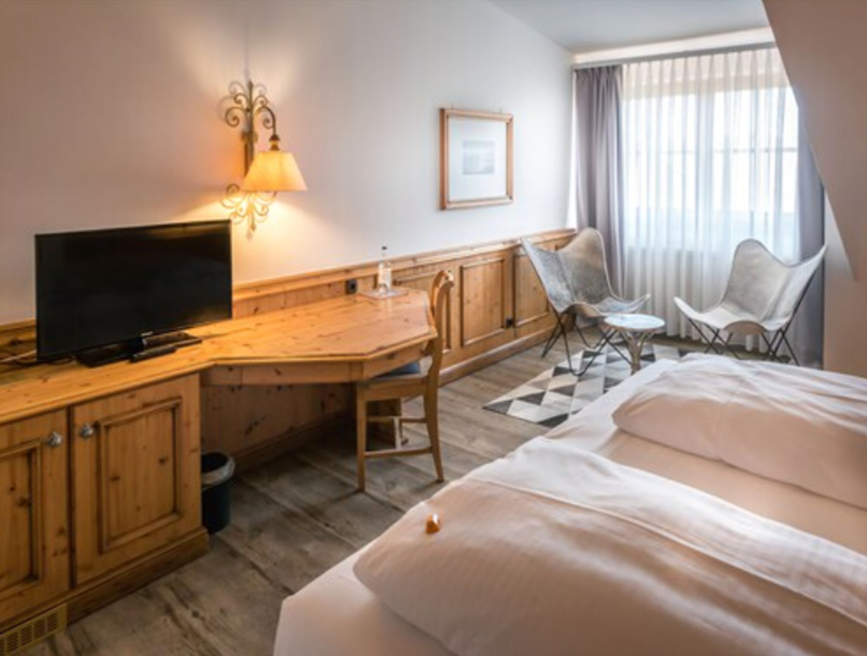 A hotel room with a wooden desk, a television, a bed, and two chairs.