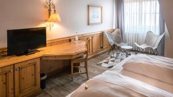 A hotel room with a wooden desk, a television, a bed, and two chairs.