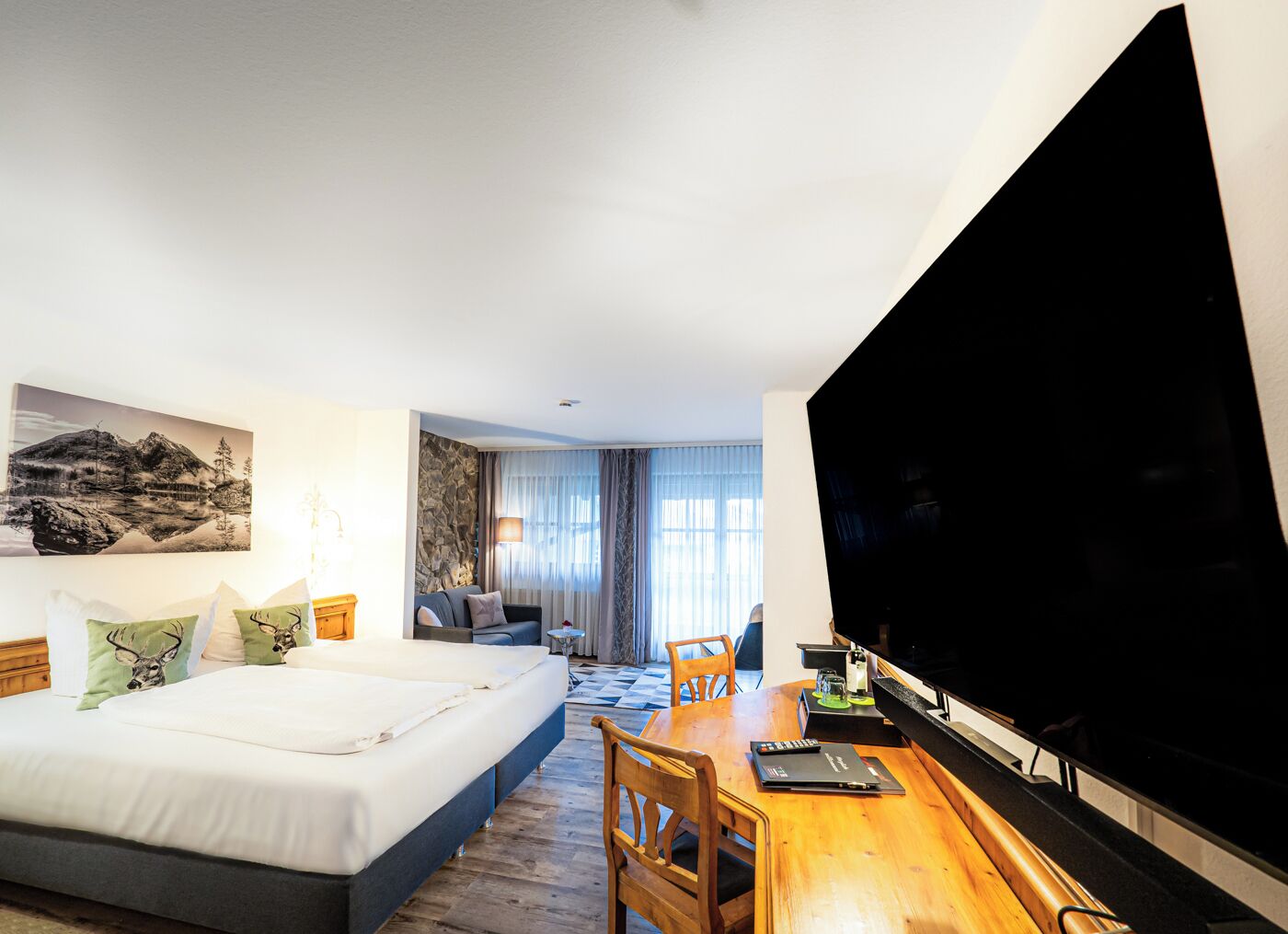 A hotel room with a bed, a desk, a TV, and a painting on the wall.