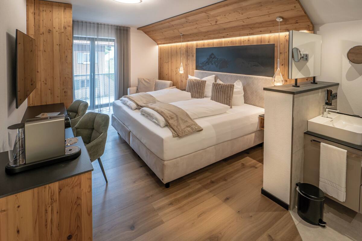 A modern bedroom with a large bed, a desk with a computer, and a bathroom with a sink and mirror.