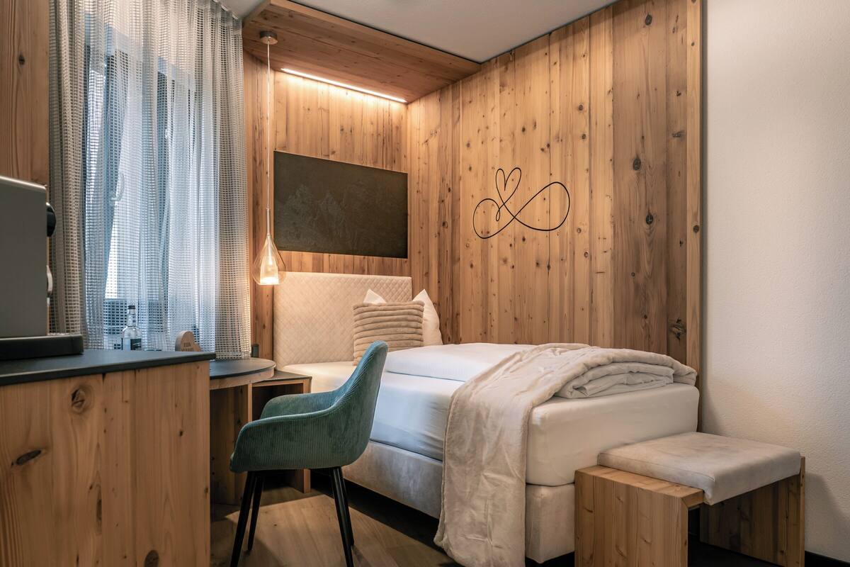 A bedroom with a bed, bedside table, chair, and a wall with a heart design.