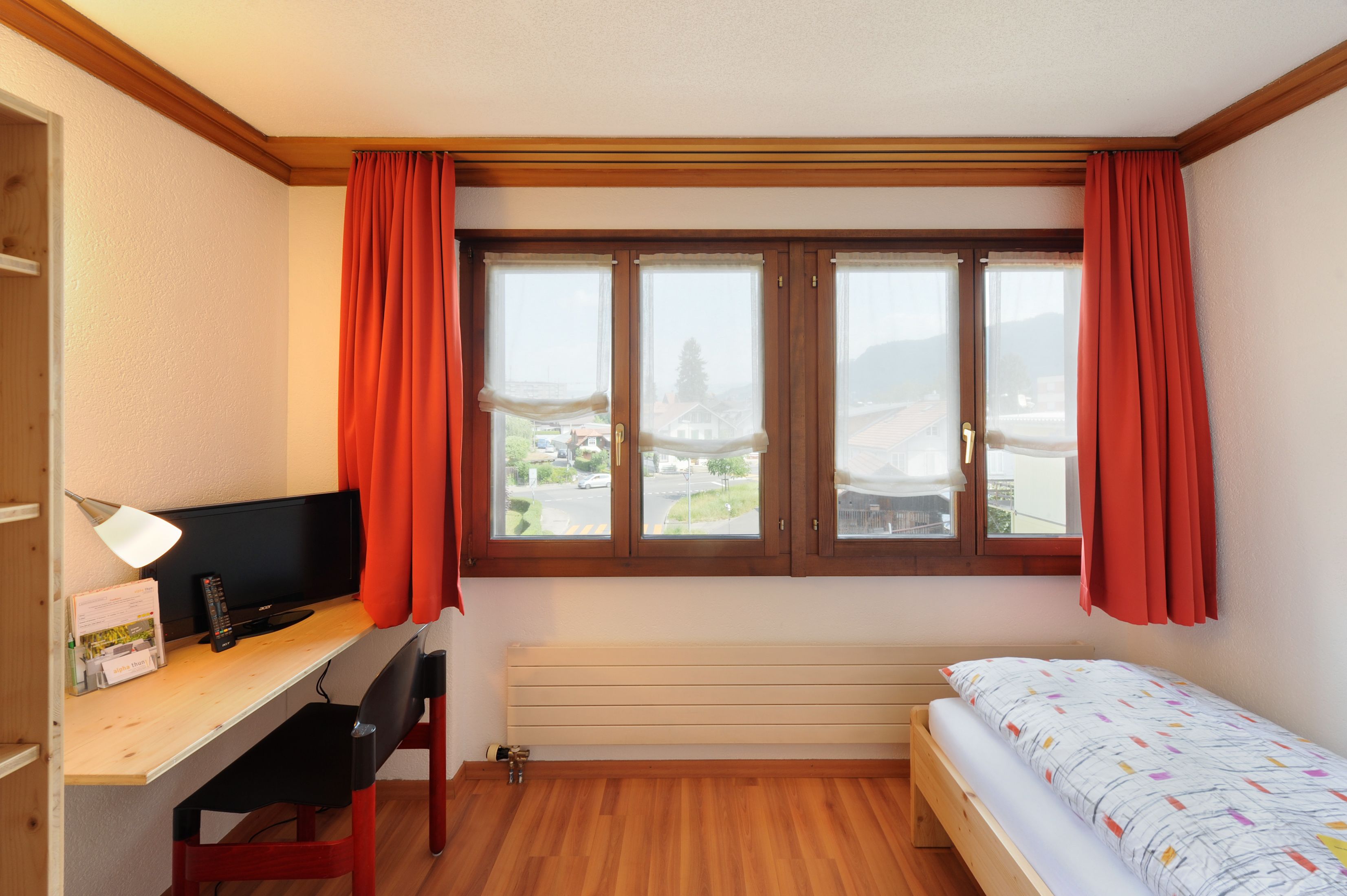 A bedroom with a wooden desk, a bed, and a window with curtains.
