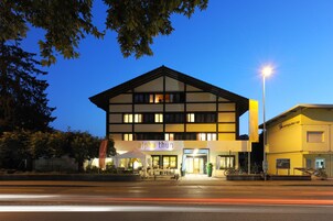 Un edificio moderno con un letrero que dice "alpha thun" en la entrada, que presenta una fachada bien iluminada y un cielo despejado al fondo.