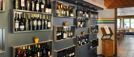 A wine cellar with shelves of wine bottles, a wooden cabinet, and a dining area in the background.
