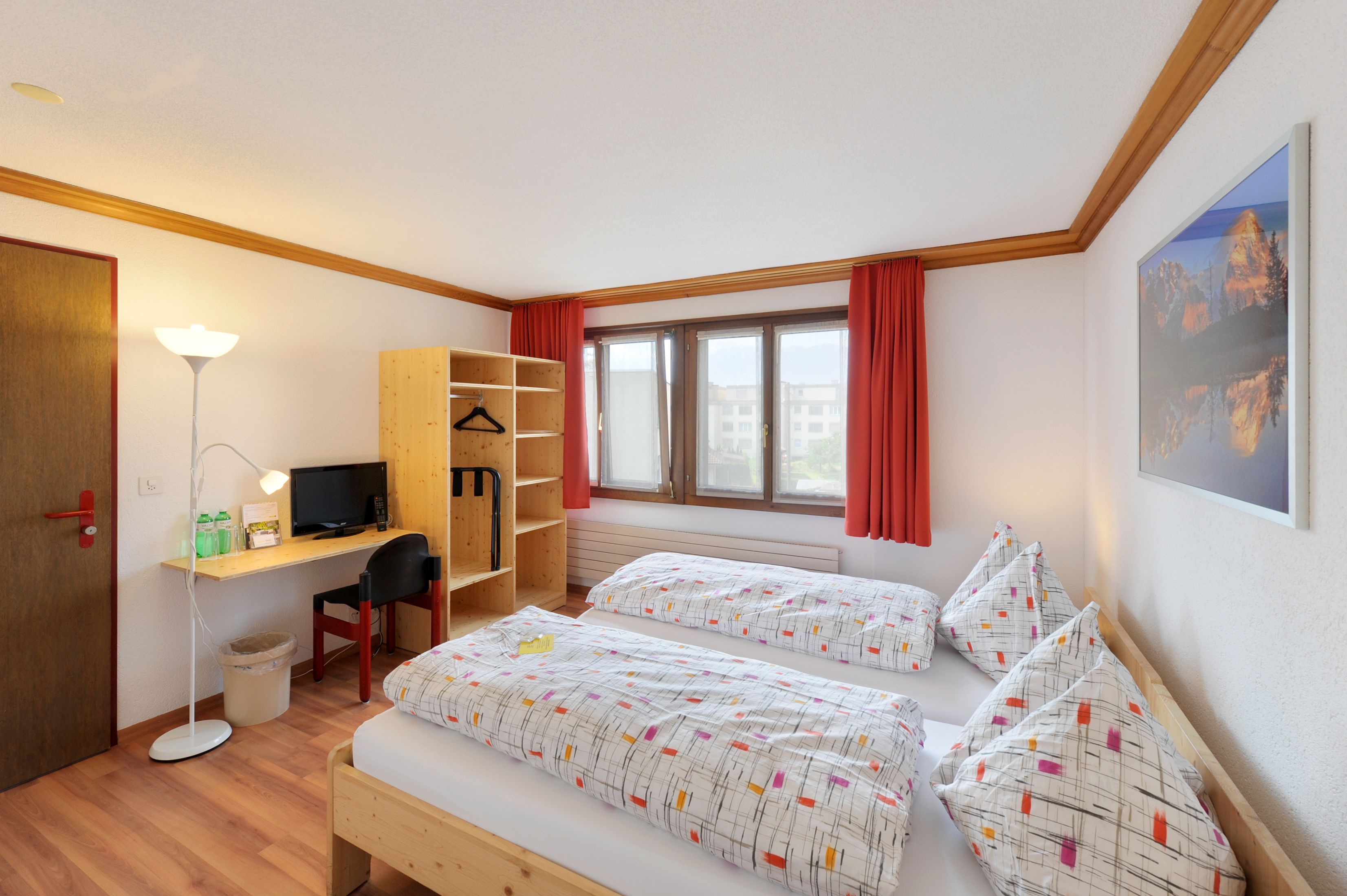 Un dormitorio con dos camas, un escritorio con computadora, una silla, una lámpara de pie y una ventana con cortinas.