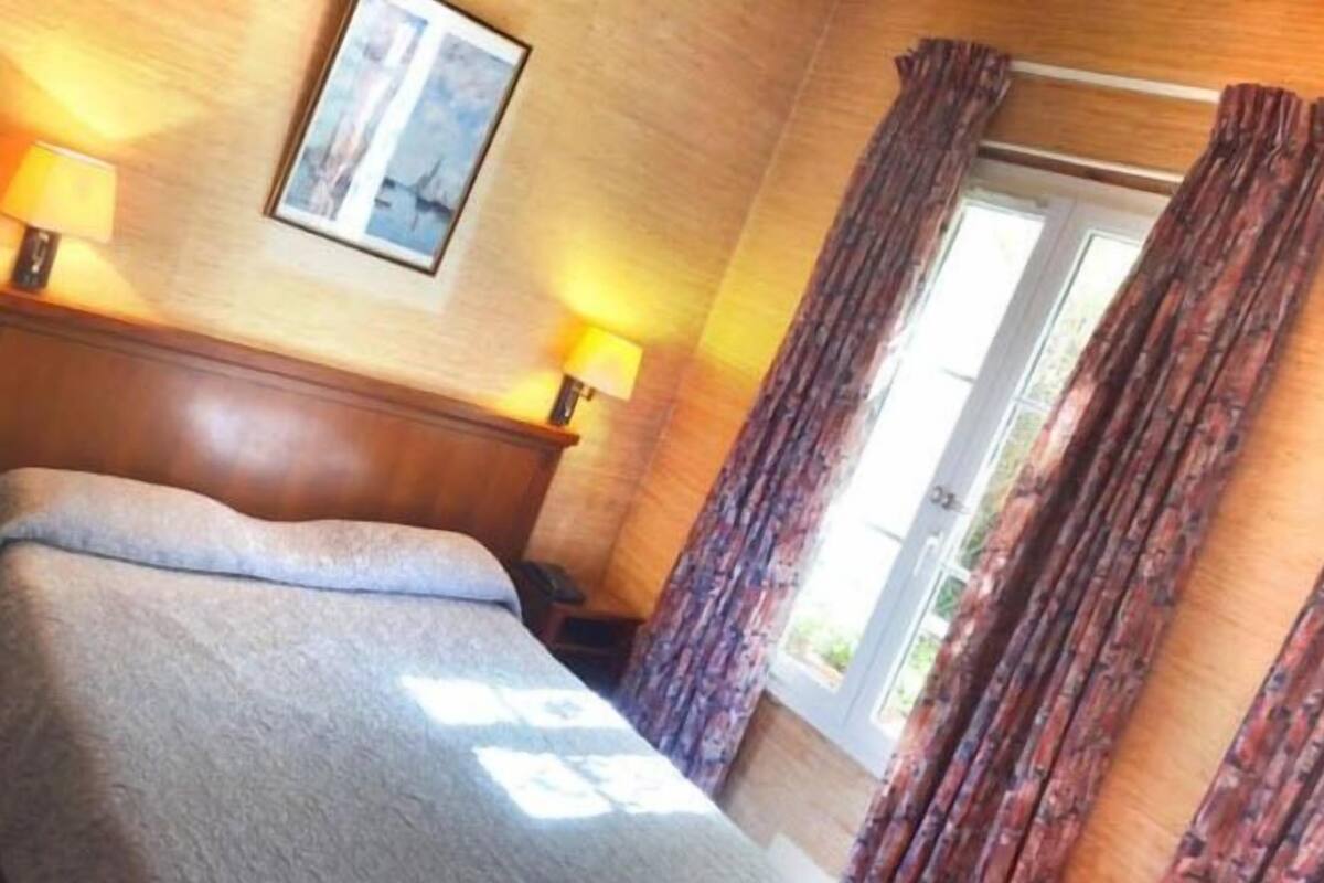 A hotel room with a bed, two bedside lamps, a framed picture on the wall, and a window with curtains.