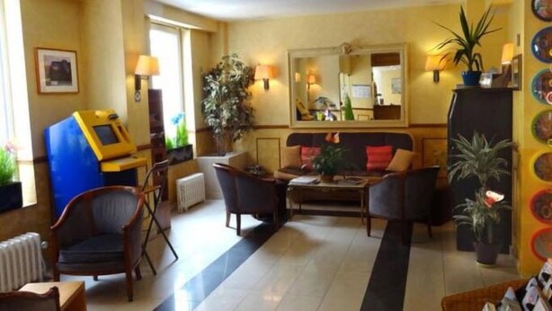A hotel lobby with a reception desk, seating area, and a large mirror. - Villa Du Maine (Paris)