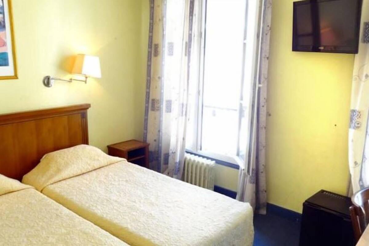 A hotel room with two beds, a bedside lamp, a television, and a window with curtains.