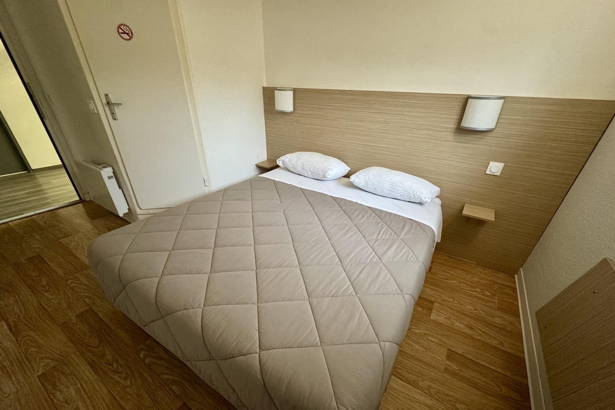 A neatly made bed with a beige quilt, two pillows, and a wooden headboard.