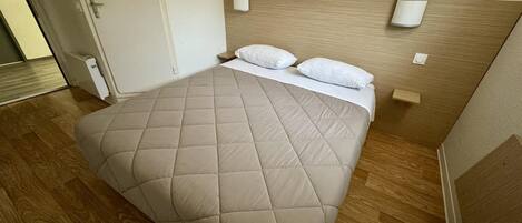 A neatly made bed with a beige quilt, two pillows, and a wooden headboard.